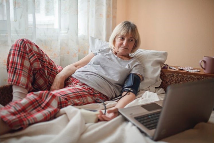 A senior patient lying on his bed, having a virtual checkup with her doctor
