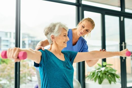 A woman asssisting a senior woman in lifting weights